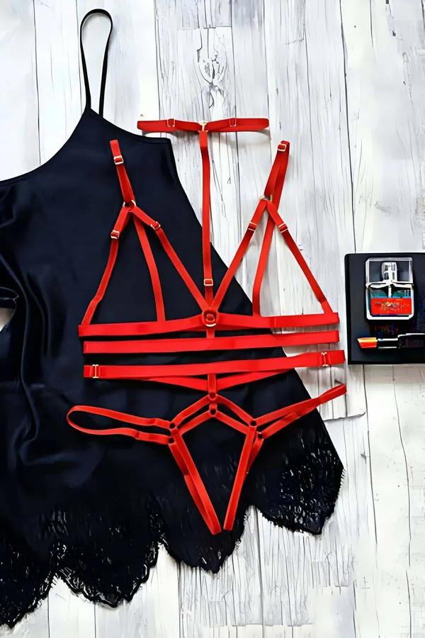 Red strappy harness bralette and cage thong lingerie set with gold-tone O-rings on white wood surface