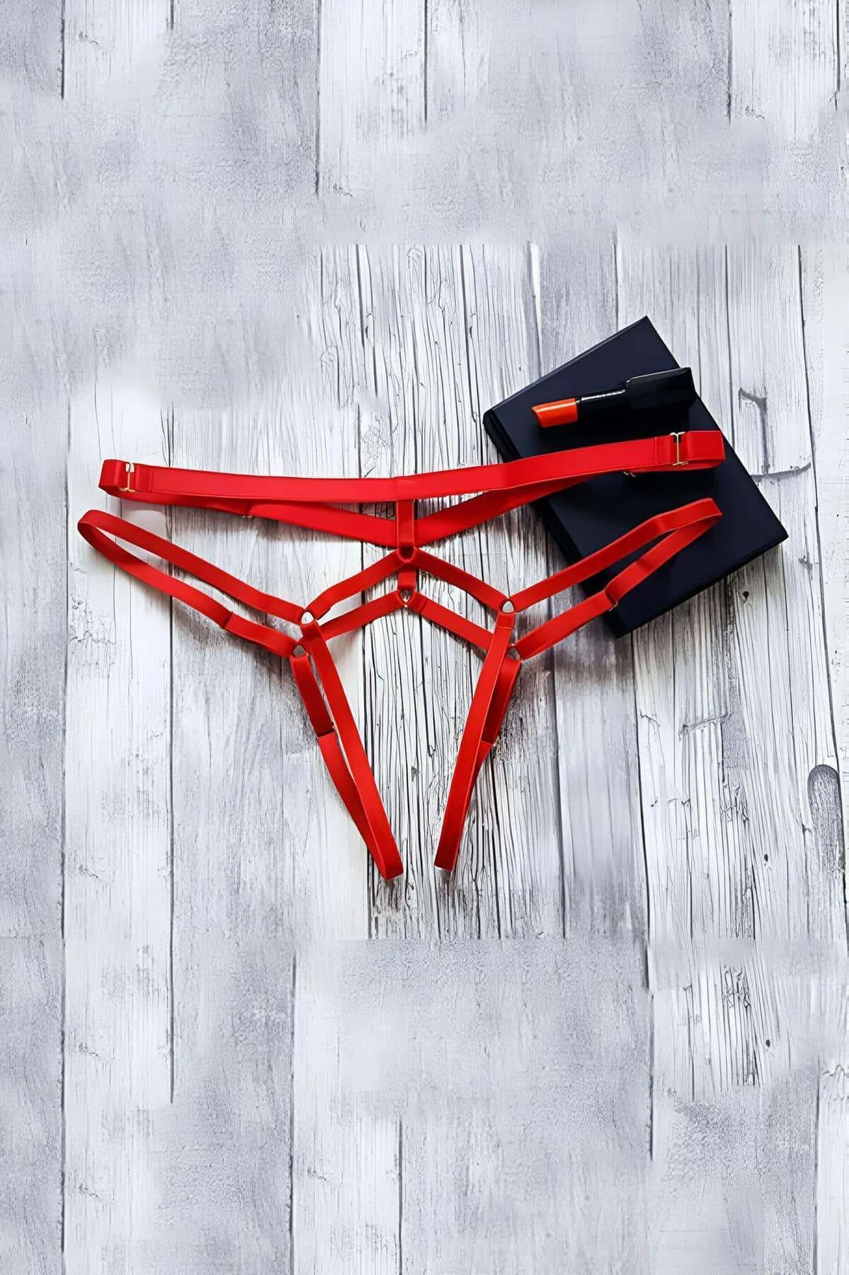 Red strappy thong harness with three elastic waist bands and gold-tone adjustable slider buckles on white wood surface