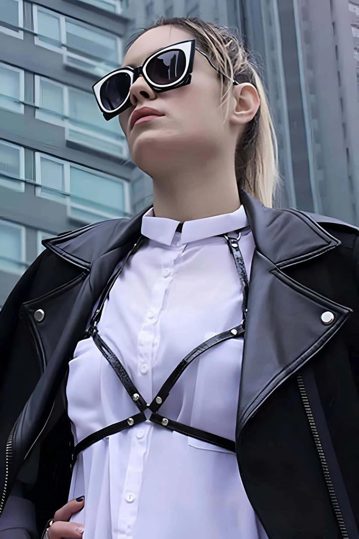Black faux leather adjustable strappy chest harness with silver hardware worn over white shirt