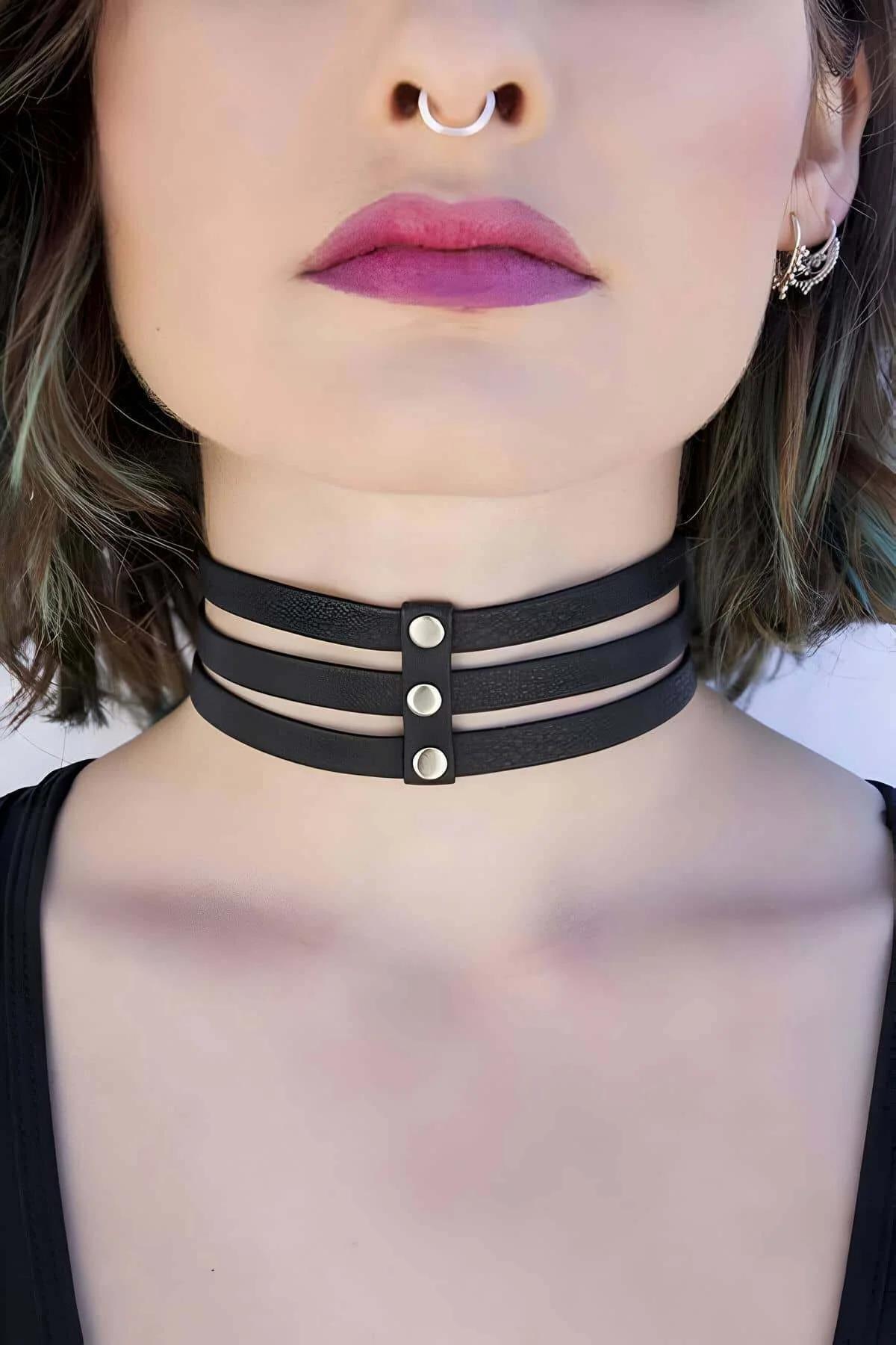 Black faux leather triple strap choker with three silver dome studs aligned at center front, worn close to the throat