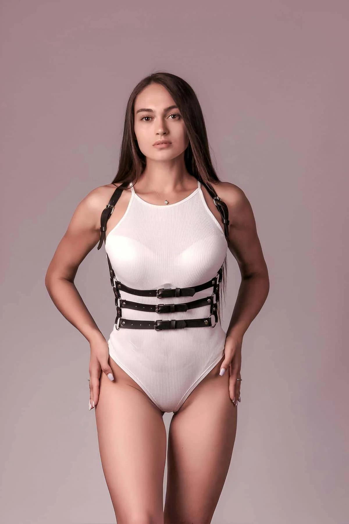 black faux leather 3-strap body harness with gold-tone buckles and D-rings worn over white ribbed bodysuit