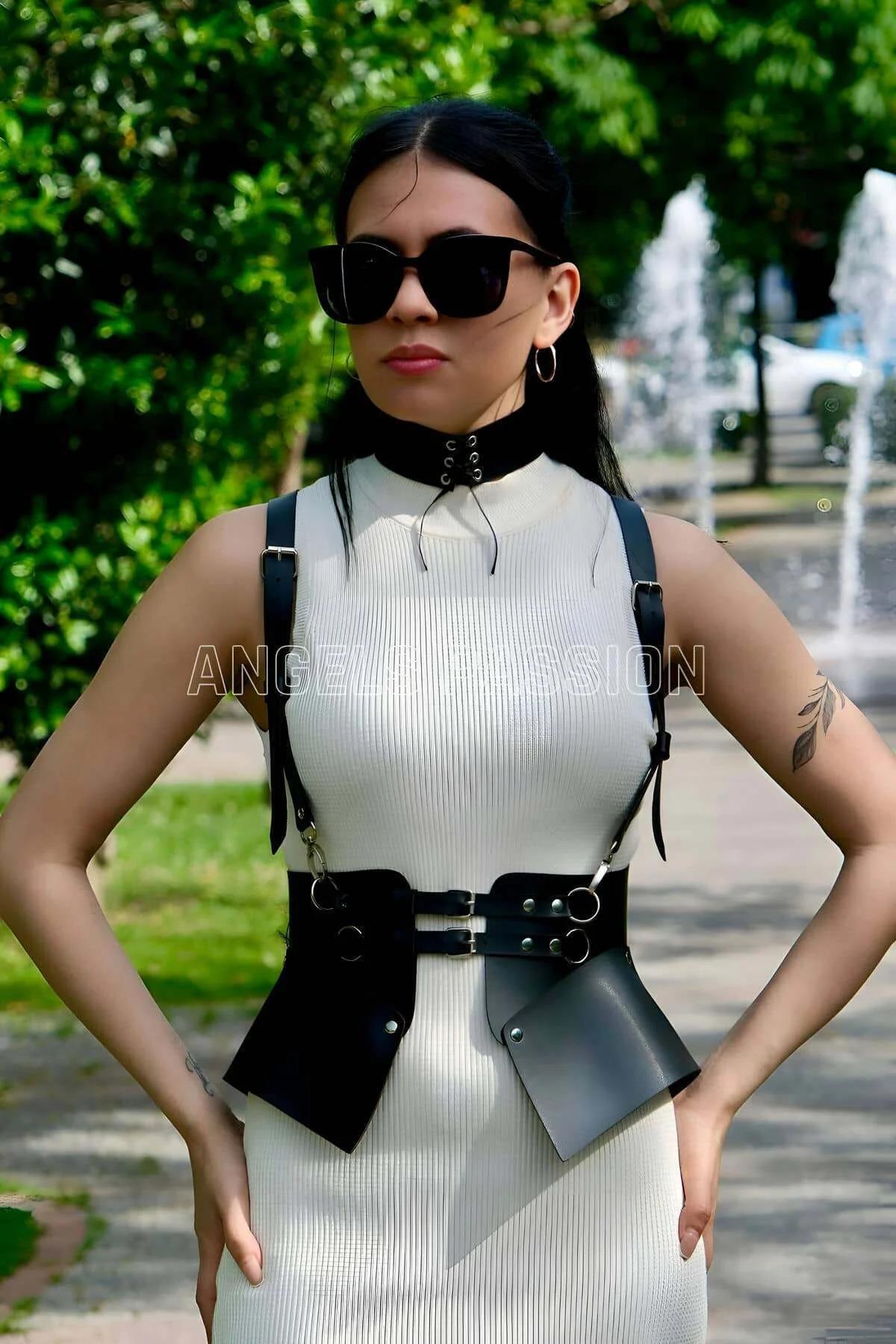 Black faux leather structured waist harness with wide peplum side panels silver O-rings and lace-up choker worn over white ri