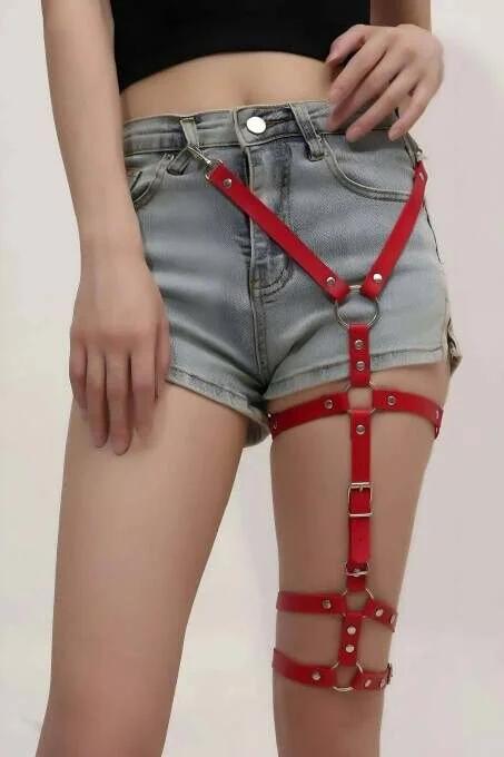 Red faux leather thigh harness with silver O-ring and four adjustable buckle strap bands worn over denim shorts