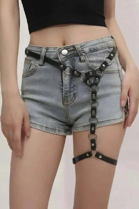 Black faux leather single leg garter harness with silver O-rings rivets and detachable chain worn over denim shorts