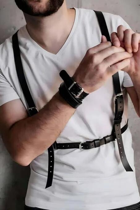 black faux leather chest harness with silver-tone buckles worn over white t-shirt, adjustable strap configuration