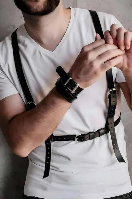 black faux leather chest harness with silver-tone buckles worn over white t-shirt, adjustable strap configuration