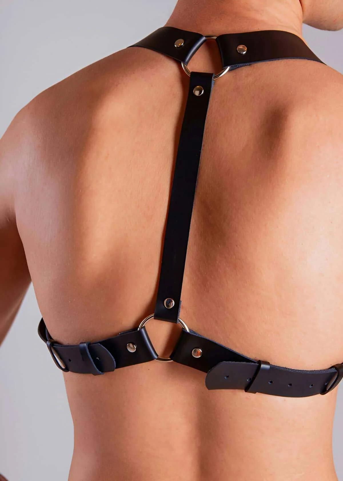 Black faux leather back body harness with silver O-rings and adjustable buckles on male torso back view