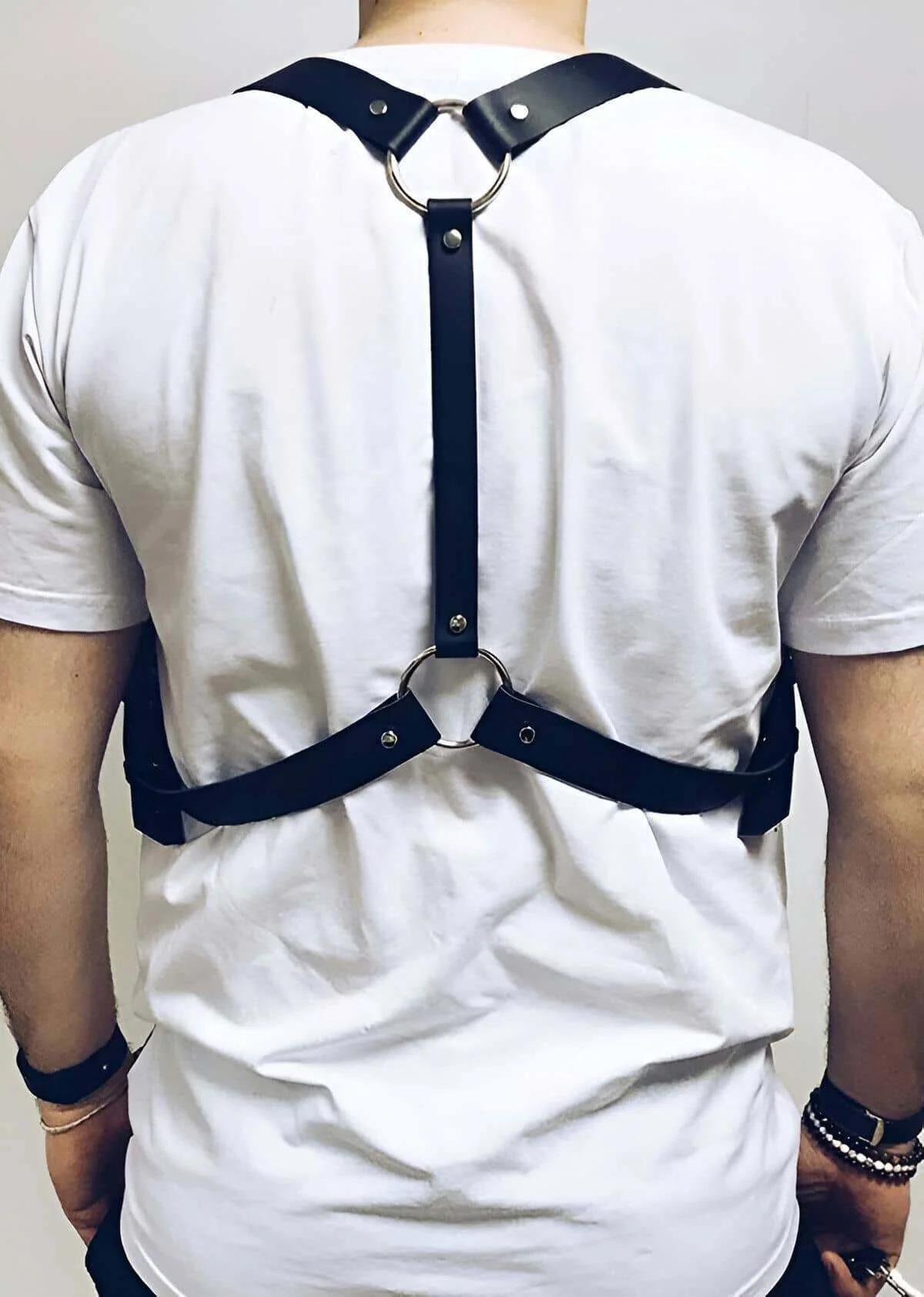 Black faux leather chest harness with two silver O-rings shown from the back on a male model wearing a white T-shirt