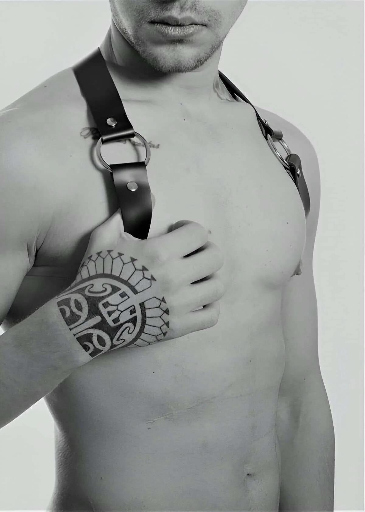 Black vegan leather shoulder harness with silver O-rings and adjustable flat straps on male torso