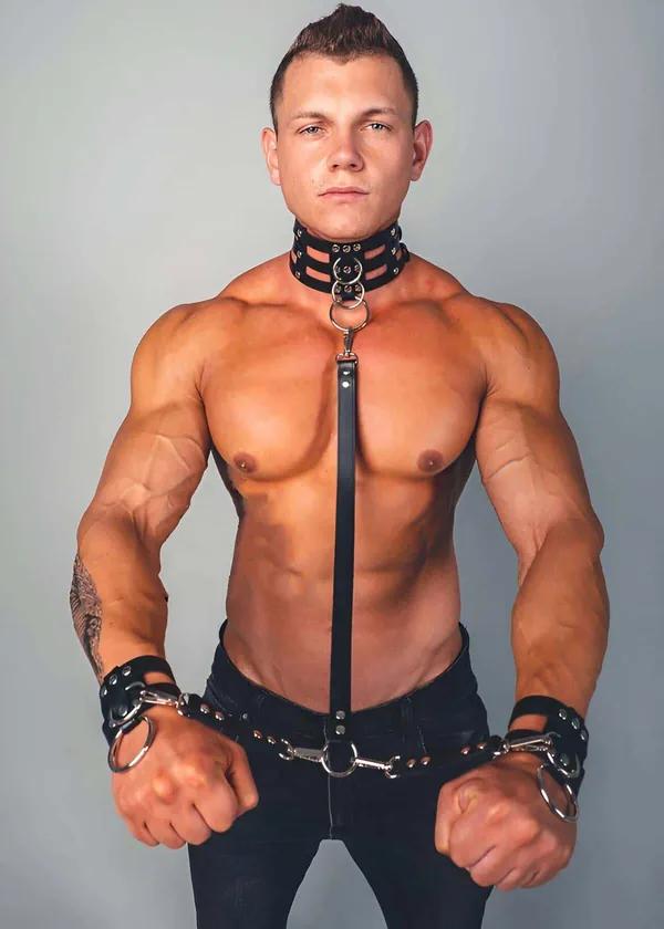 black faux leather collar cuffs and leash set with silver O-rings and stud hardware worn by male model