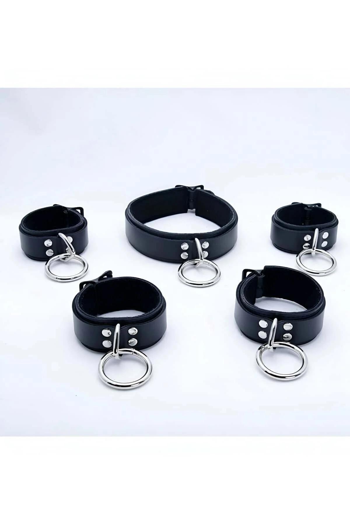 Black faux leather O-ring choker and four matching cuffs set with silver zinc alloy rings laid flat