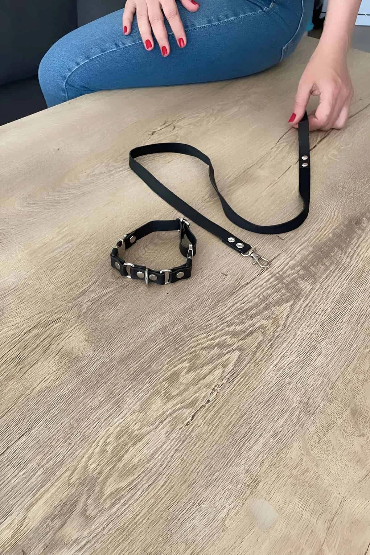 Black faux leather studded choker with silver rivets and matching flat-strap leash laid flat on wooden surface